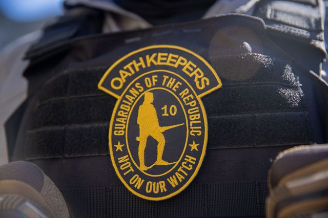 The yellow Oath Keepers logo that shows a silhouette of a man with a rifle with the words "Guardians of the REpublic, not on our watch"